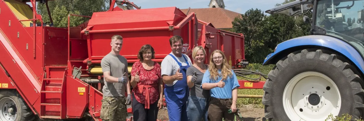 Fünf Personen stehen vor dem roten Kartoffelroder und dem blauen Traktor