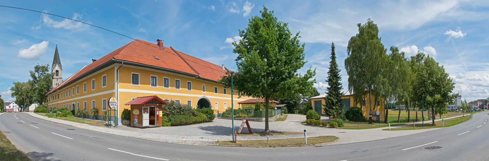 Weites Panorama des Hofs mit Kirchturm, Verkaufshütte und Straßenkreuzung